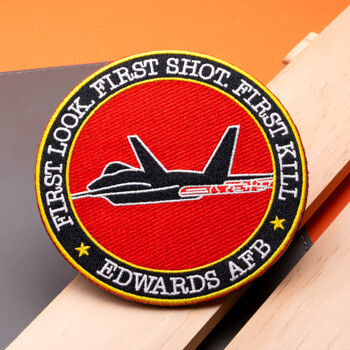 Circular embroidered patch for Edwards AFB featuring a black fighter jet silhouette on a red background with yellow and black borders.
