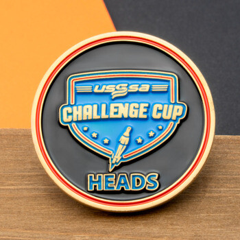 Circular challenge coin with USSSA Challenge Cup shield and Heads text in blue and gold on a black background.