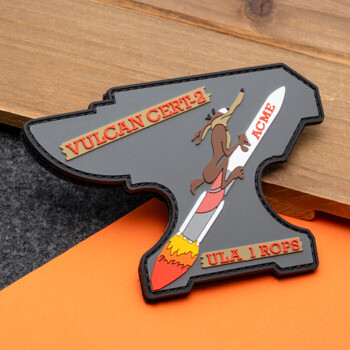 Anvil-shaped PVC patch featuring Wile E. Coyote on an ACME rocket with Vulcan Cert-2 and ULA 1 ROPS text.