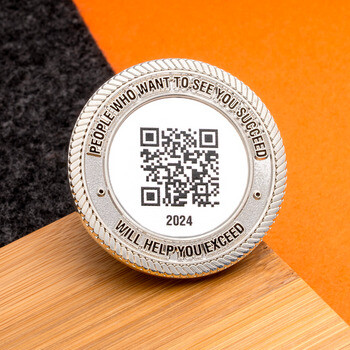 Silver challenge coin with an engraved QR code, textured rope edge, and inspirational quote.